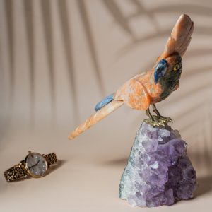 Handcrafted orange calcite parrot figurine on amethyst geode